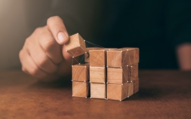business man try to build wood block on wooden table and blur background business organization startup concept